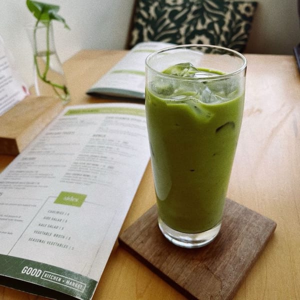 Iced green drink on a wooden coaster next to a Good Kitchen menu on a light wooden table.