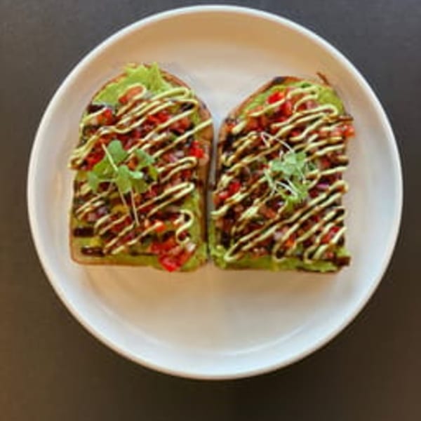 Two slices of avocado toast with diced tomatoes, balsamic glaze, and microgreens on a white plate.